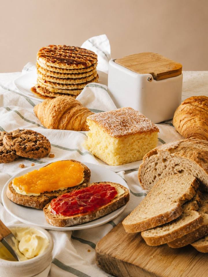 Mesa de lanche com pães integrais, bolo, croissants, biscoitos e torradas com geleia